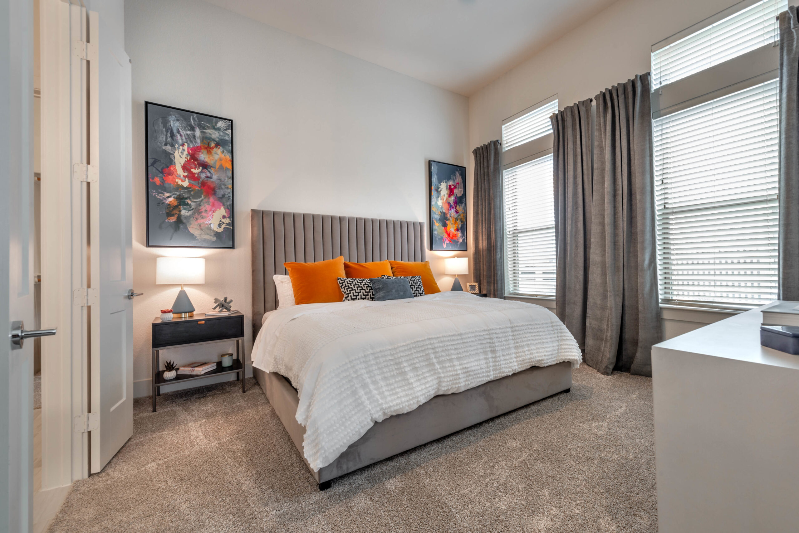 Model bedroom at our apartments in Fort Worth featuring colorful art, large windows, and a queen sized bed.